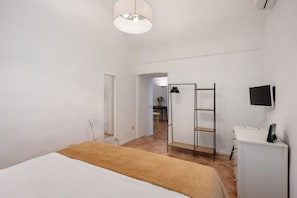 A bedroom with a bed, a desk with a monitor, a chair, and a wardrobe.