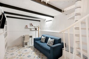 Een kamer met een blauwe bank, een witte stoel, een bureau en een trap.