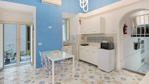 Une cuisine compacte avec des meubles blancs, un four à micro-ondes et un grille-pain. On y trouve une table à manger avec des chaises et une petite plante en pot.
