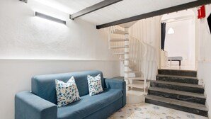 Un canapé bleu agrémenté de coussins à motifs, un escalier avec une rampe blanche et un sol à motifs.