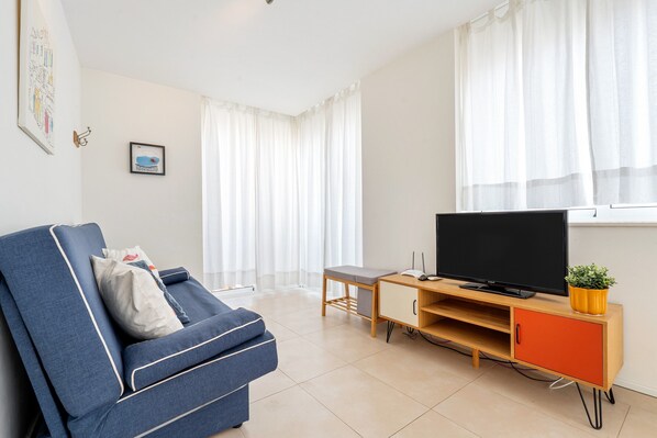 Una sala de estar con un sofá, un televisor sobre un mueble de madera, una mesita y una ventana con cortinas.