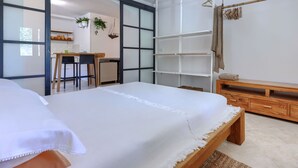 Ein Schlafzimmer mit einem Bett, einer Holzbank, einem Schreibtisch und einem Stuhl. Es gibt einen Kleiderschrank mit Spiegel und einer Hängepflanze.