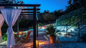 Eine Außenpatio mit Steinböden, einer Pergola mit weißen Vorhängen, einem Pool und einer Treppe.