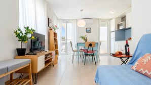 A modern living room with a sofa, a TV, a dining table with chairs, a kitchen area, and a balcony view. - Apartment 'Sf1' with Wi-Fi and Air Conditioning (L'Ametlla de Mar)