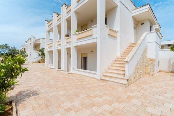 A multi-story building with balconies, a stone staircase, and a paved courtyard.