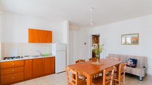 Een keuken met houten kastjes, een eettafel, stoelen, een bank en een hanglamp.