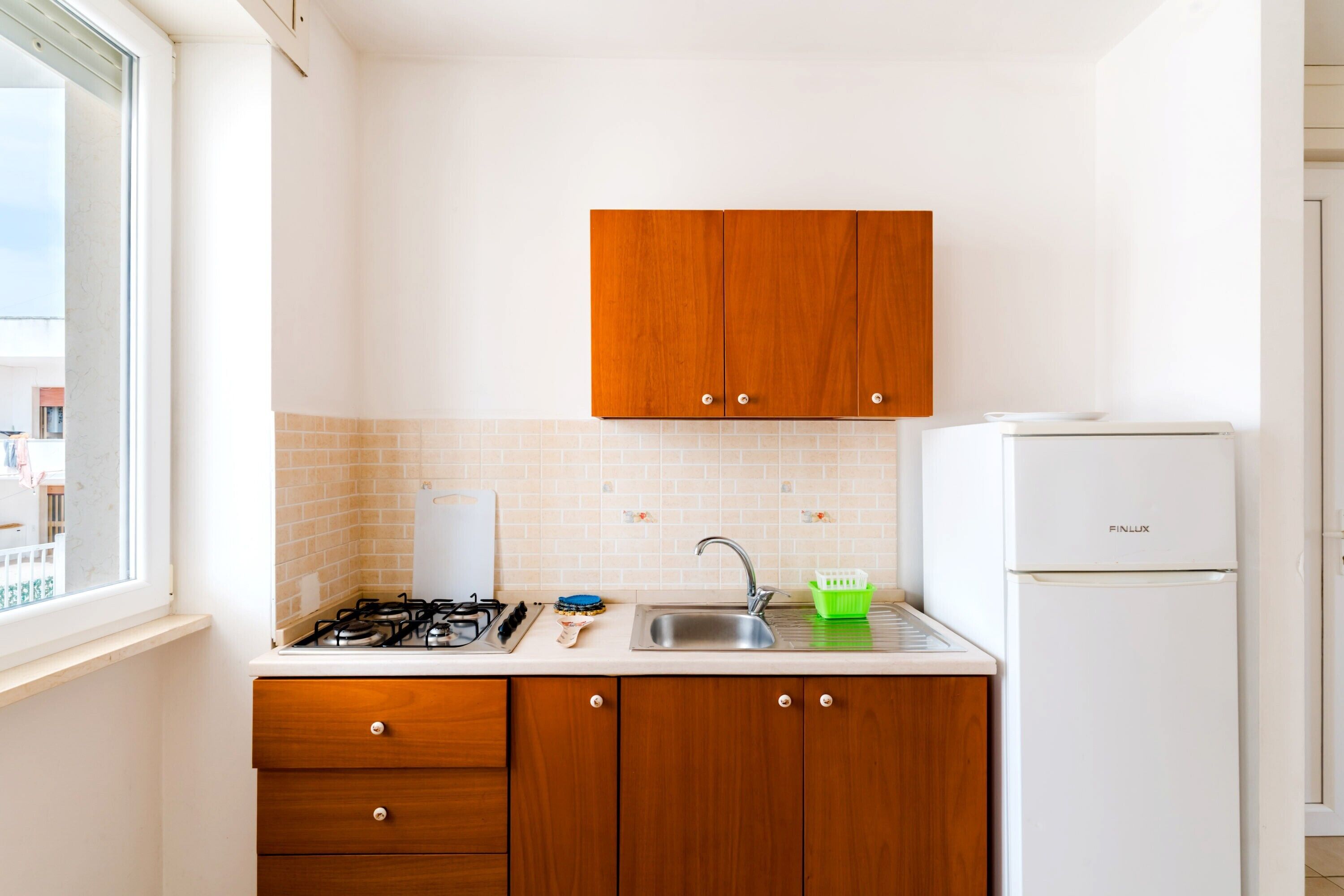 Een keuken met houten kastjes, een gasfornuis, een spoelbak en een witte koelkast.