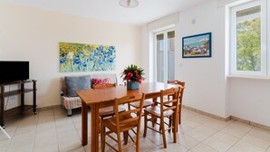 Un área de comedor con una mesa y sillas de madera, un sofá, un mueble para televisión y obras de arte en las paredes.