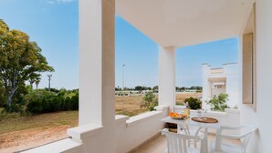 Un balcón con mesa y sillas, vista al campo y un edificio blanco.