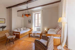Una habitación acogedora con sofá, cama de madera, una mesita, sillas de mimbre y una lámpara colgante.