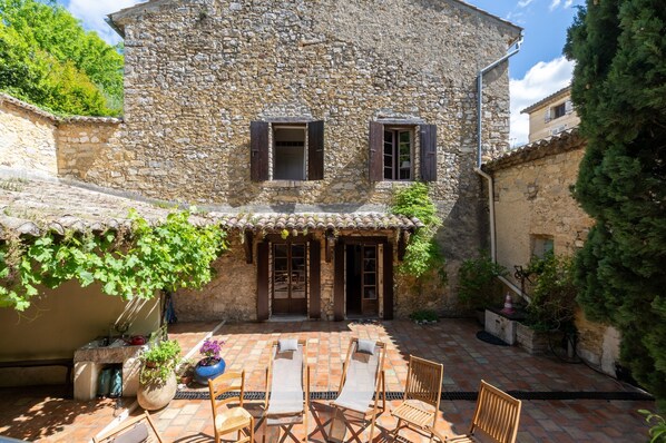 Edificio de piedra con patio, mesas al aire libre y un pequeño jardín.