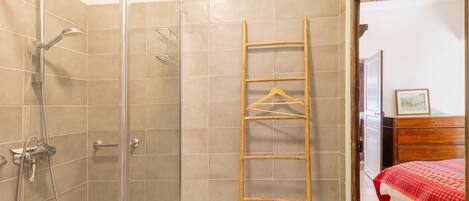A bathroom with a shower, a wooden ladder, and a bed with a red blanket.