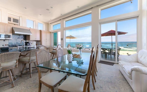 Cocina amplia con ventanas grandes, comedor con mesa de vidrio y vista al océano.