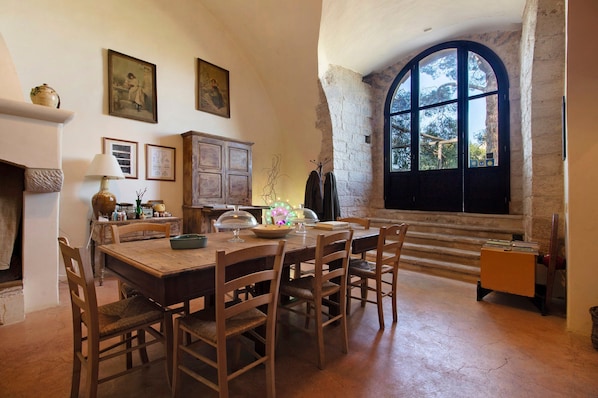 A dining area with a wooden table and chairs, a fireplace, and a large arched window.
