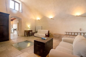 A spacious living area with a high ceiling, a white sofa, a wooden coffee table, and a stone fireplace.