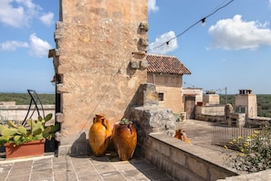 A rooftop terrace with stone walls, two large vases, a cactus plant, and a small garden area.