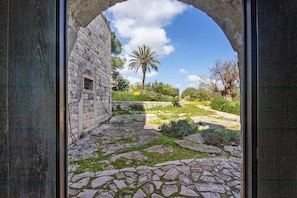 An arched stone doorway leading to a courtyard with a palm tree and a stone building.