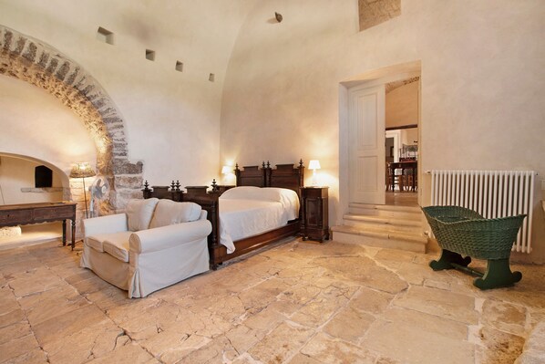 Une chambre avec un sol en pierre, un lit, une chaise et une lampe.