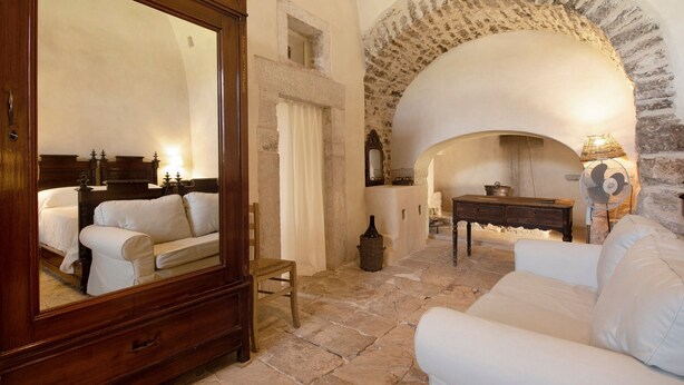 A room with a stone fireplace, a mirror, a white sofa, a wooden cabinet, and a small table with a lamp.