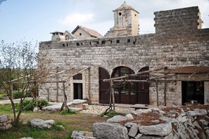 Un bâtiment en pierre doté d’entrées en arc de cercle, d’un clocher et d’une cour intérieure parsemée de rochers et de quelques plantes.