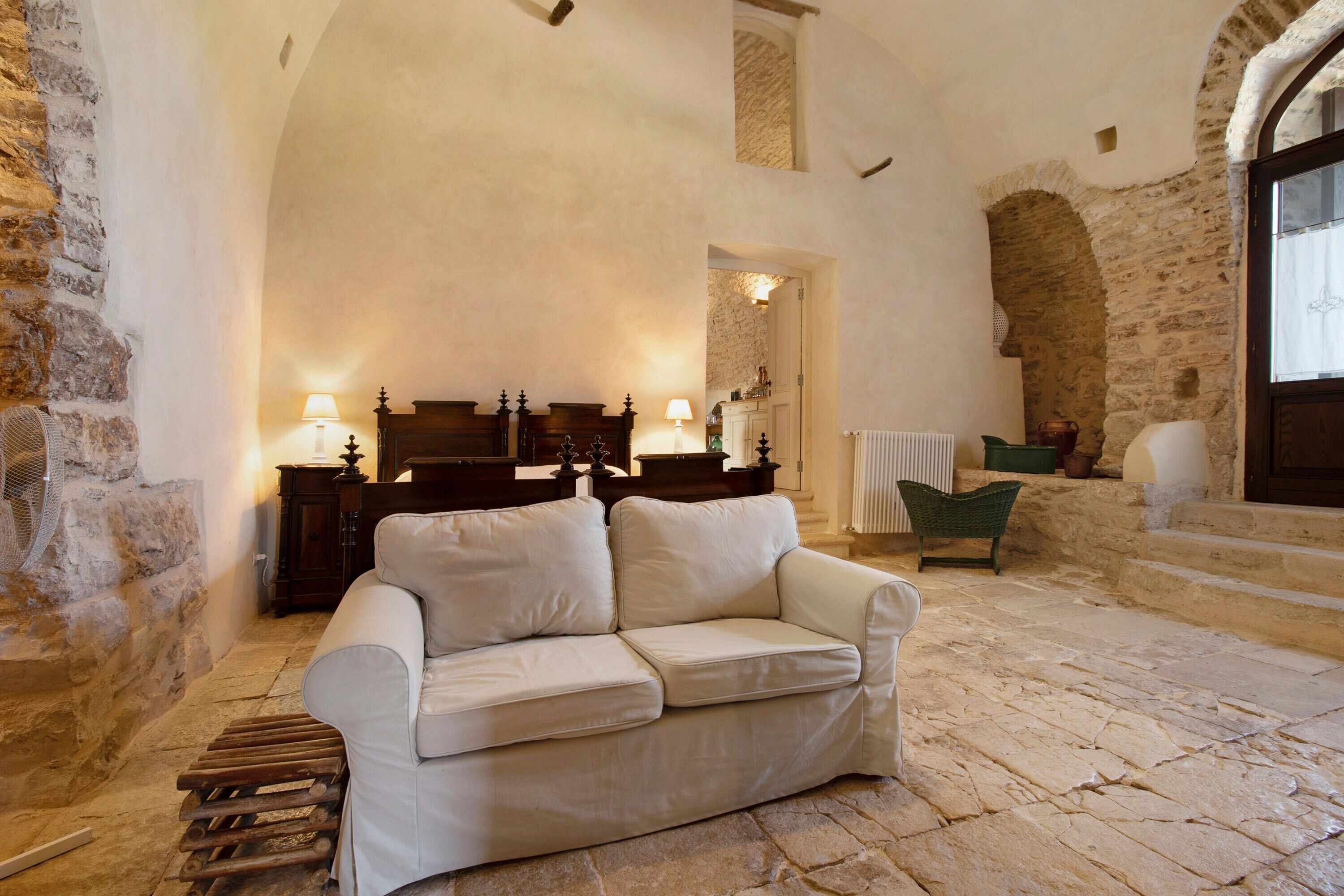 A stone-floored room with a white sofa, wooden furniture, and a stone wall.