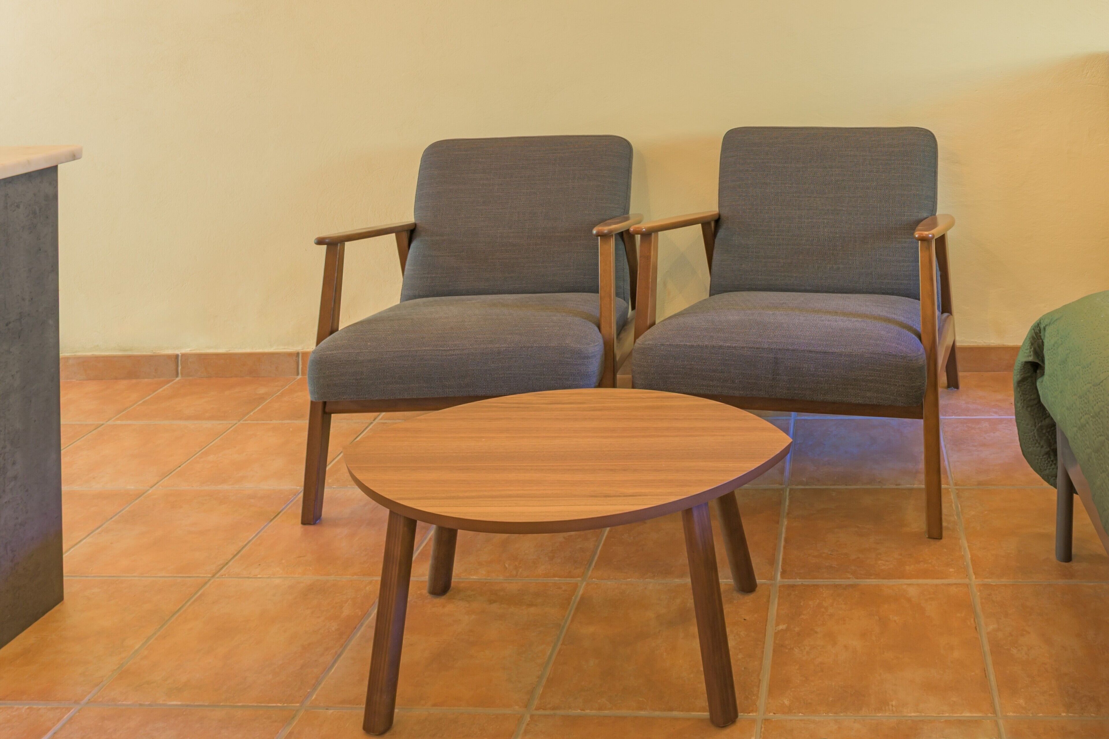 Twee fauteuils met houten poten en een klein houten tafeltje in een kamer met betegelde vloer.