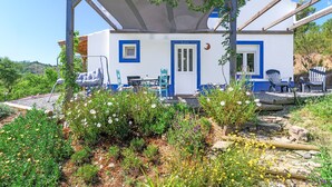 A white building with blue accents, a covered patio area, and a garden with various plants and flowers.