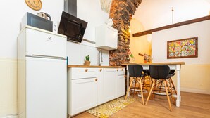 Une cuisine compacte avec un réfrigérateur blanc, un four à micro-ondes et une cuisinière, un coin repas avec une table et des chaises, et un mur en pierre.