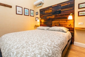 Un dormitorio con cabecera de madera, cama con ropa de cama estampada, luces fijadas a la pared y cuadros enmarcados.
