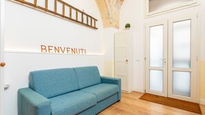 Une pièce avec un canapé bleu, une échelle en bois, une porte avec des panneaux en verre dépoli et le mot « BENVENUTI » écrit sur le mur.