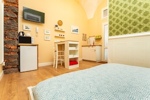 Une chambre à coucher comprenant un lit, une petite kitchenette, un téléviseur, une horloge et une fenêtre avec des rideaux à motifs.