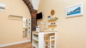 Ein Zimmer mit Holzboden, einem weißen Schreibtisch mit Stuhl, einem an der Wand montierten Fernseher, einer Uhr und einem gerahmten Bild.