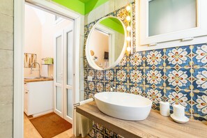 Une salle de bain avec un lavabo rond, un miroir avec éclairage intégré et un mur recouvert de carreaux à motifs.
