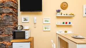 Eine kompakte Küche mit Mikrowelle, kleinem Kühlschrank, Holzausstattung, einem an der Wand montierten Fernseher und einer Uhr.