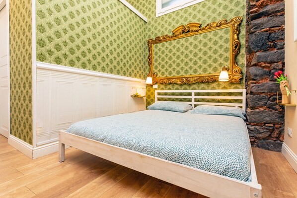 Une chambre à coucher avec un lit, un mur en pierre, un miroir et un papier peint à motifs.