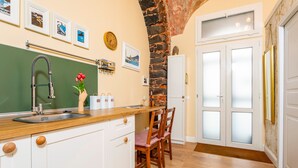Een keuken met een houten aanrecht, witte kasten, een stenen muur en een eethoek met stoelen.