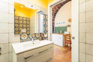 Un baño con lavamanos blanco, espejo y azulejos estampados.