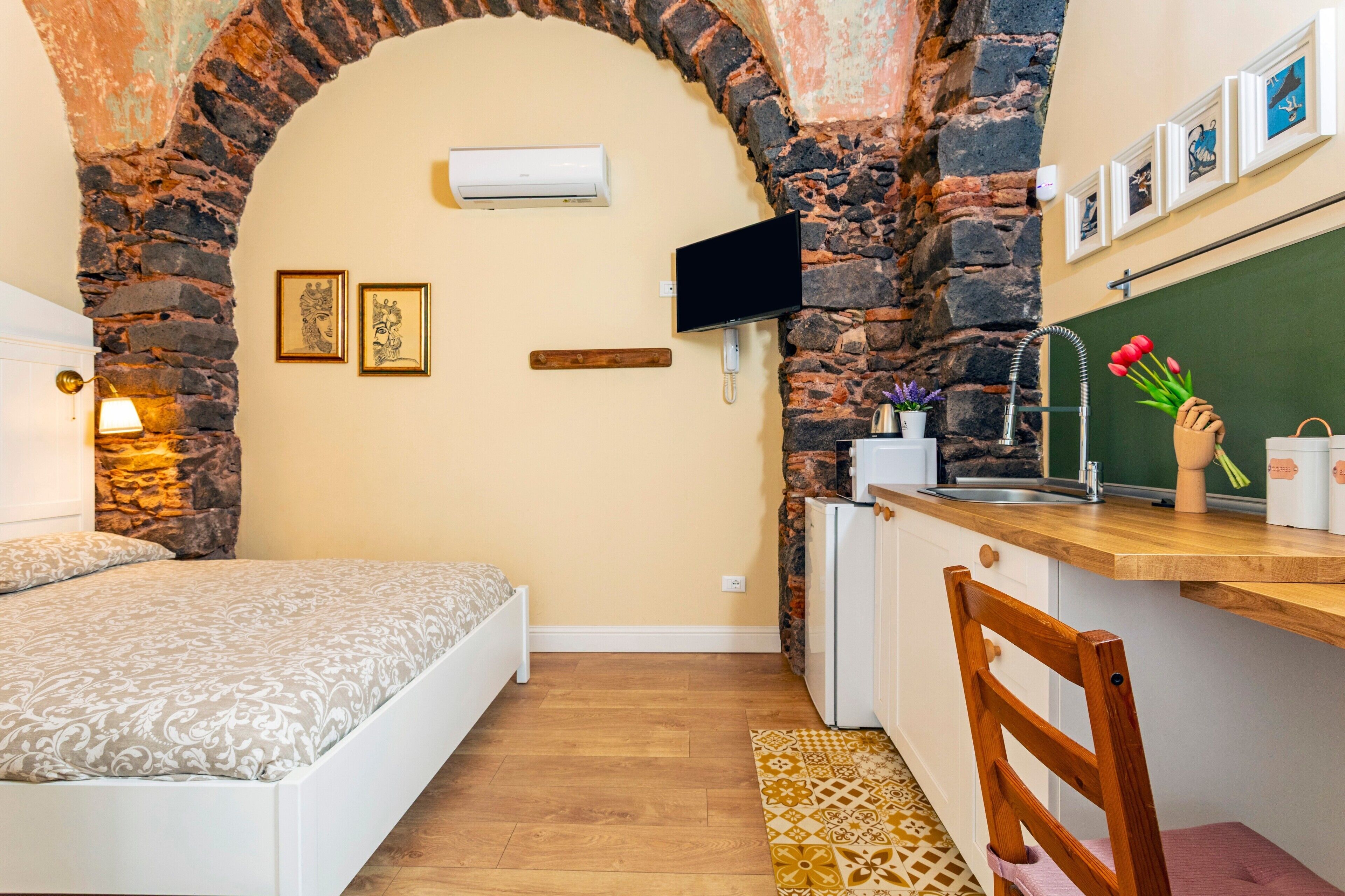 Ein kleiner Raum mit Bett, Schreibtisch, Stuhl, einer Mini-Küche und einem Steinbogen.