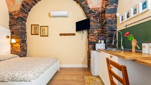 Een compacte kamer met een bed, een bureau, een stoel, een klein keukenhoekje en een stenen boog.