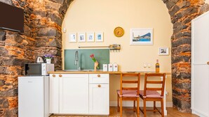 Een kleine keuken met een stenen muur, een magnetron, een spoelbak en een houten eettafel met stoelen.