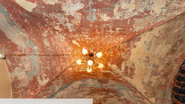 Een plafond met afbladderende verf en een kroonluchter.