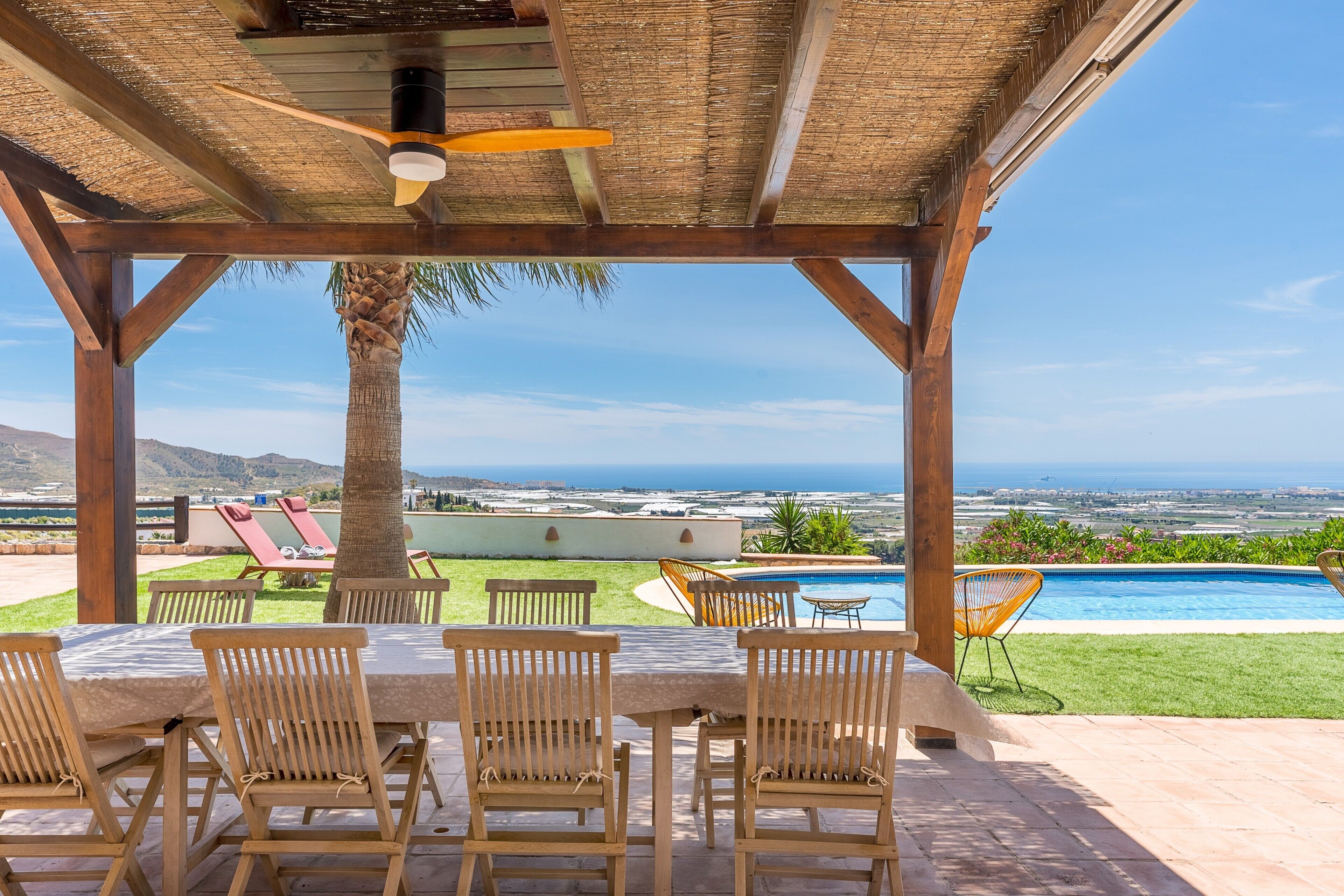 Un espacio al aire libre cubierto con piscina, sillas de madera y una mesa.