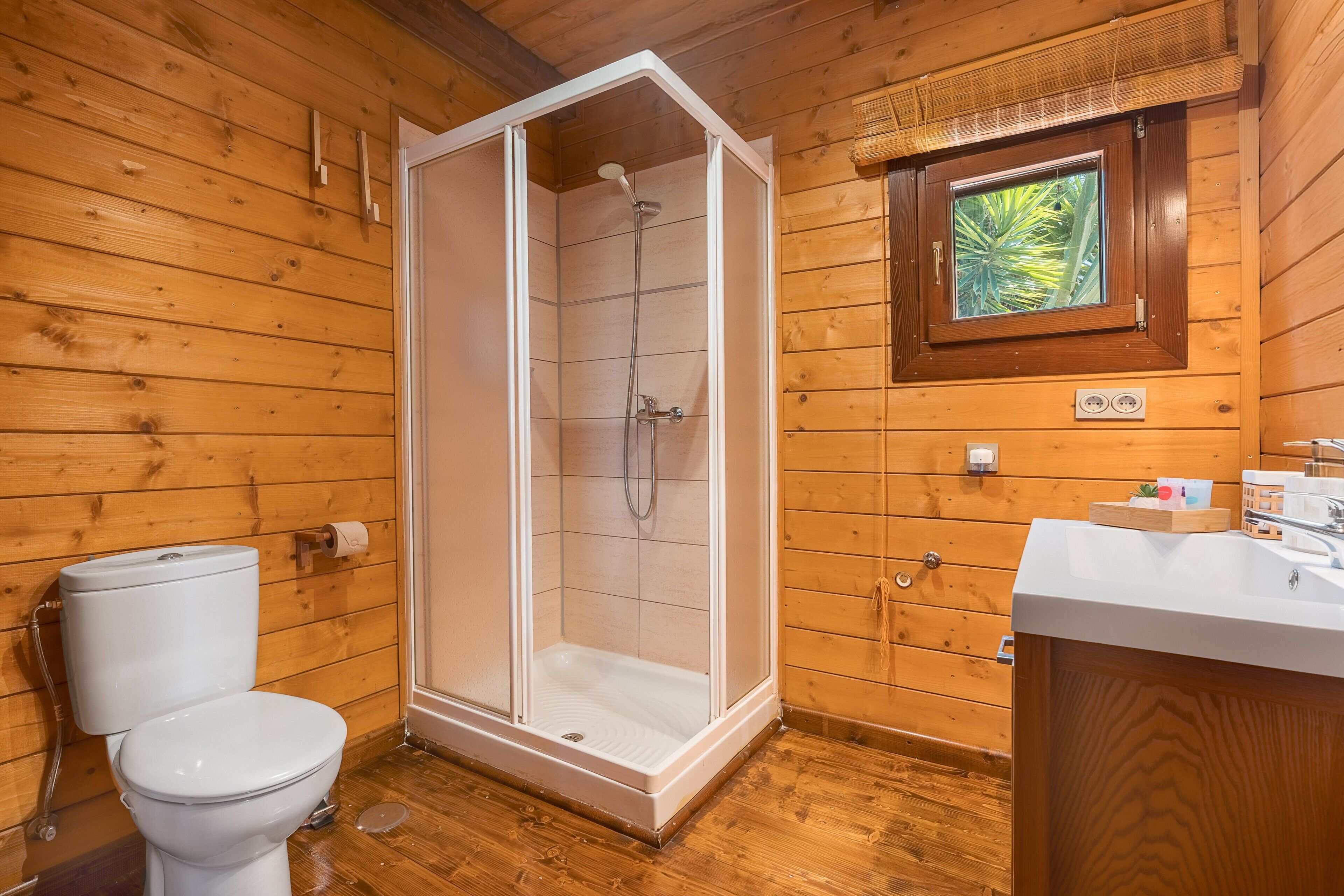 A wooden cabin bathroom with a shower, toilet, and sink.