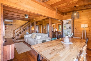 A wooden cabin interior with a dining table, sofa, and staircase.