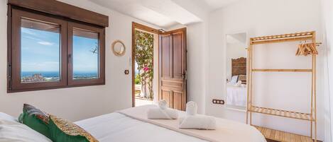 A bedroom with a bed, a wooden wardrobe, a window with a view, and a door leading to a balcony.