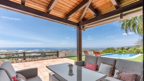 A covered patio with wicker furniture, a glass table, and a view of the sea and landscape. - Holiday Home 'La Haima' with Sea Views, Wi-Fi and Air Conditioning (Motril)