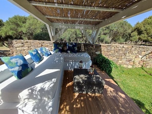 An outdoor seating area with a pergola, stone wall, and lush greenery. - Casa Rural Maximon Green Apartment – Forest, Peace & Atlantic Views (Los Caños de Meca)