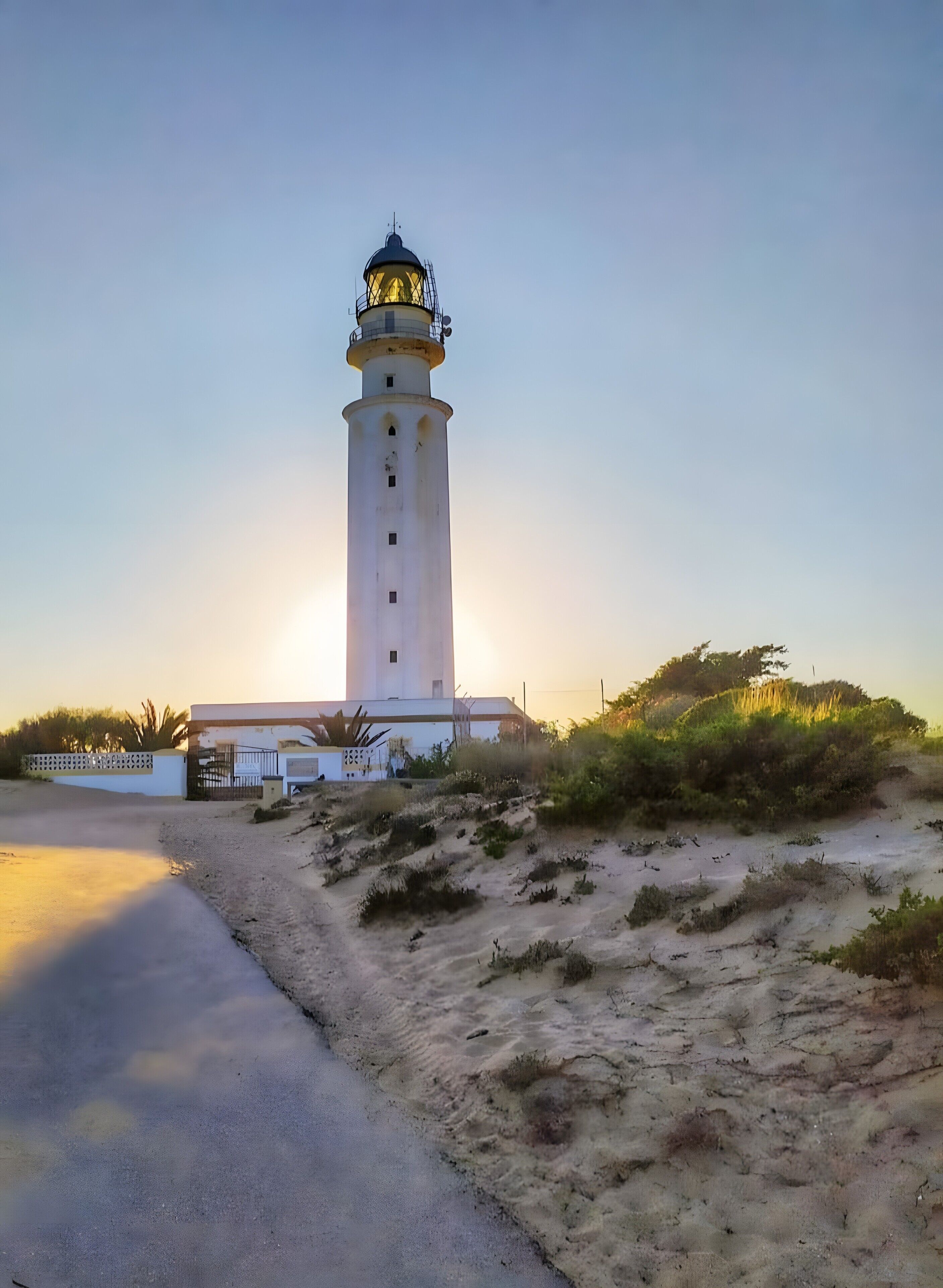 Un phare doté d’une tour blanche et d’une partie supérieure jaune, situé sur une zone sablonneuse où la végétation est clairsemée.