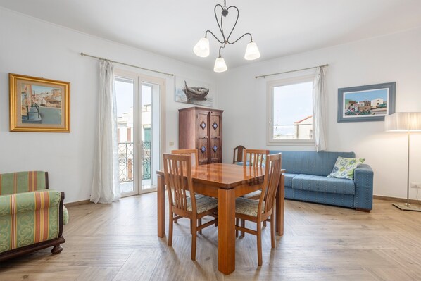 Un comedor con una mesa y sillas de madera, un sofá azul, un aparador y una araña.