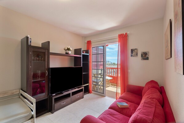A living room with a flat-screen TV, a red sofa, a cabinet with glass doors, and a sliding glass door leading to an outdoor area.